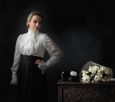 Portrait of a woman in retro clothes. White blouse with lace, embroidery and high collar. On a table...