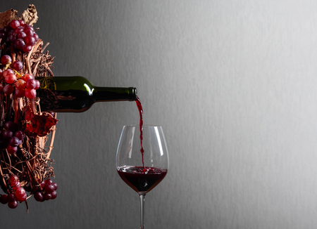 Red wine pouring from a bottle into a glass. Wreath of vine with juicy grapes. Conceptual image on the theme of winemaking. Copy space for your text.の写真素材