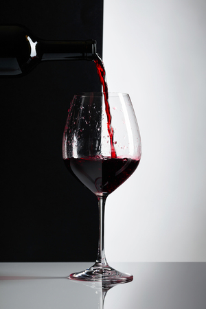 Red wine is poured into a glass. Reflexive background, copy space for your text.の写真素材