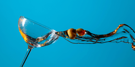 Dry martini with green olives on a blue background. Cocktail in glass with splashes. Copy space for your text.の写真素材