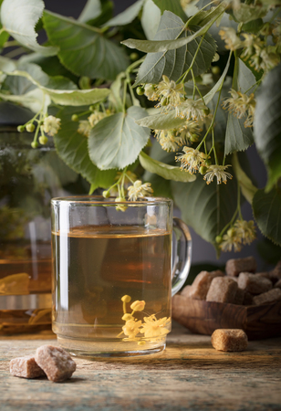 Glass of linden tea with brown sugar and flowers on wooden table.の写真素材