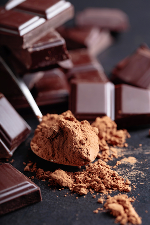 Broken chocolate pieces and cocoa powder on black background.の写真素材
