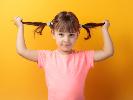 Four-year-old girl in a pink t-shirt on an orange background. Hair tied in a ponytails.の写真素材