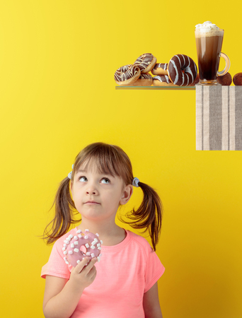 Girl in a pink t-shirt eat donut and look up. Yellow background, copy space.の写真素材