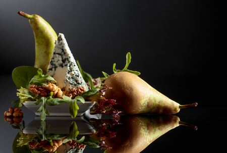 Blue cheese with walnuts, pear and greens on a black background.の写真素材