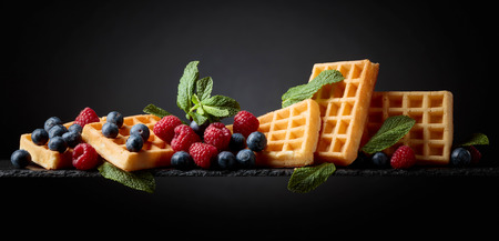 Belgian waffles with  blueberries, raspberries  and fresh mint a dark background.