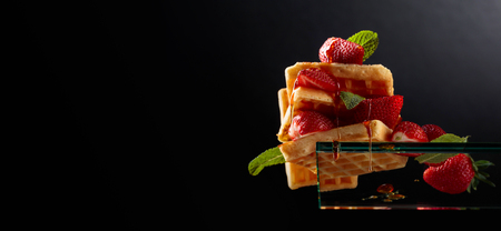 Belgian waffles with strawberries and honey garnished with fresh mint. Waffles on a glass shelf, bottom view.  Copy space.の写真素材