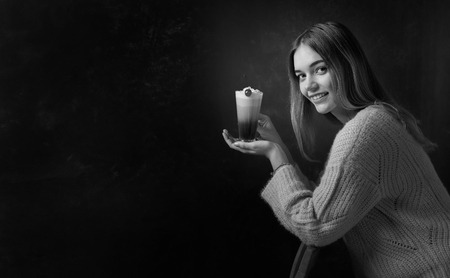 Beautiful smiling girl in a sweater holding a coffee cocktail with cream garnished with cherry. Copy space for your text. Black and white.の写真素材