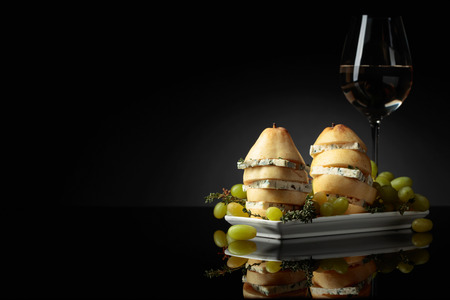 Blue cheese with pear, thyme and grapes on a black reflective background. Blue cheese and white wine. Copy space.の写真素材