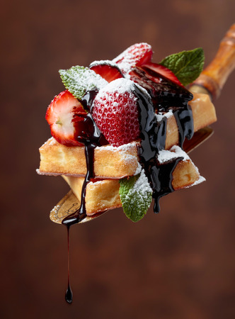 Belgian waffles with strawberries, mint and chocolate sauce, sprinkled with powdered sugar.の写真素材