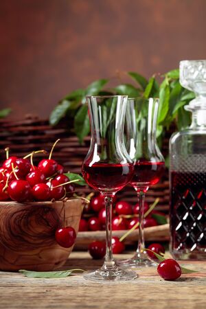 Cherry liquor and red cherries in a wooden bowl on a wooden table in garden. Wicker fence with green leaves in the background.の写真素材