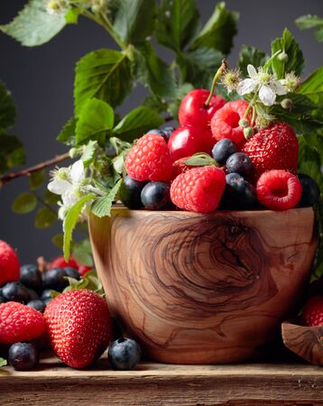 Berries closeup colorful assorted mix of strawberry, blueberry, raspberry and sweet cherry on a old wooden table. Various juicy berries with leaves.の写真素材