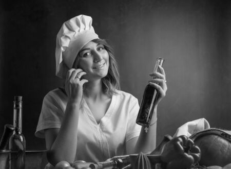Young woman in a chef uniform with small bottles of olive oil. Fragrant olive oil with various spices and herbs. Black and white.の写真素材