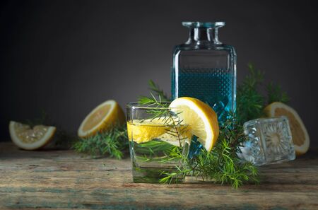 Blue gin , tonic and lemon on a old wooden table. Carbonated alcoholic drink with lemon slices and juniper branch.の写真素材