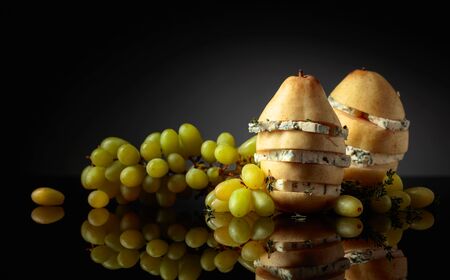 Blue cheese with pear, thyme and grapes on a black reflective background. Copy space.の写真素材
