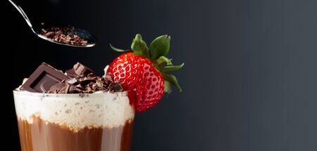 Chocolate drink with whipped cream, strawberry and pieces of black chocolate on a dark background. Copy space.の写真素材