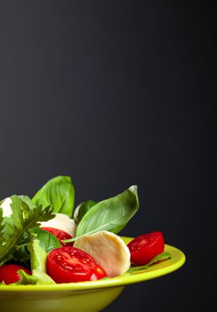 Green salad with mozzarella, tomato, basil and olive oil in green plate. Copy space. Selective focus.の写真素材