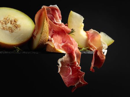 Prosciutto with melon and rosemary  on a black background, copy space.の写真素材