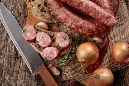 Dry-cured sausage with thyme, onion, garlic and pepper. Sausage with bread and spices on a old wooden table. Top view.の写真素材