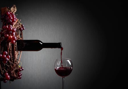 Red wine pouring from a bottle into a glass. Wreath of vine with juicy grapes. Conceptual image on the theme of wine making. Copy space for text.の写真素材