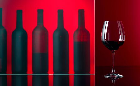 Bottles and glass of red wine on a red background. Free space for text. Focus on foreground.の写真素材