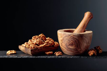 Walnuts in wooden dish and mortar with pestle on a black background. Copy space.の写真素材