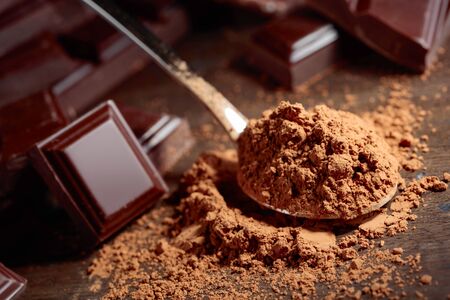 Broken  chocolate pieces and cocoa powder in small spoon on a wooden background.の写真素材