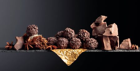 Chocolate truffles with broken pieces of chocolate and spices. Chocolate, cinnamon sticks and anise on a dark background. Copy space.の写真素材