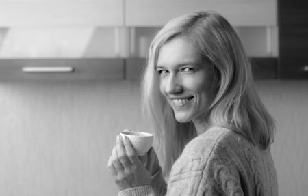 Close-up portrait of a beautiful mid age woman with cup of coffee. Attractive and happy blonde in sweater drinks coffee. Copy space. Black and white.の写真素材