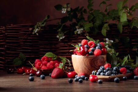 Berries closeup colorful assorted mix of strawberry, blueberry, raspberry and sweet cherry on a old wooden table in garden. Various juicy berries with leaves.の写真素材