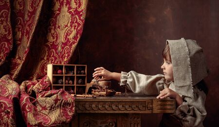 Little girl in an vintage linen dress near the table with sweets. Chocolate and spices on an old...