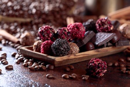 Various chocolates in wooden dish. Sweets with cinnamon sticks and coffee beans on a brown table.