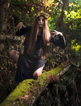 Young woman with long hair in suit of witch in forest. Halloween time.の写真素材