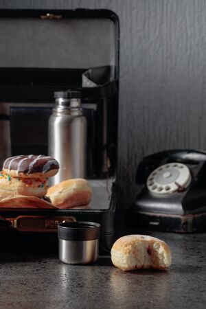 Still life in noir style. Old black phone and unfinished lunch. Donuts and flask in case.