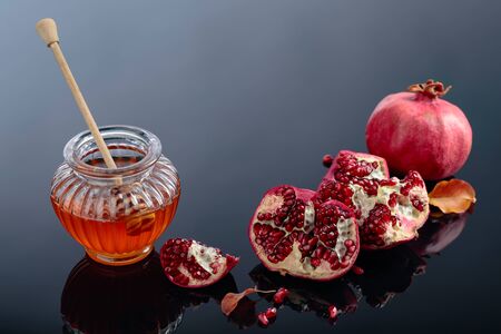 Ripe pomegranate fruits with honey and dried up leaves on a black reflective background.の写真素材