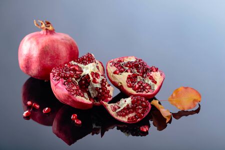 Ripe pomegranate fruits with dried up leaves on a black reflective background.の写真素材