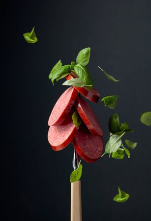 Sliced smoked sausage with green basil leaves on a fork.の写真素材