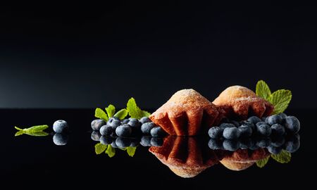 Muffins sprinkled with sugar powder on a black reflective background. Blueberry muffins with berries and mint. Copy space.の写真素材