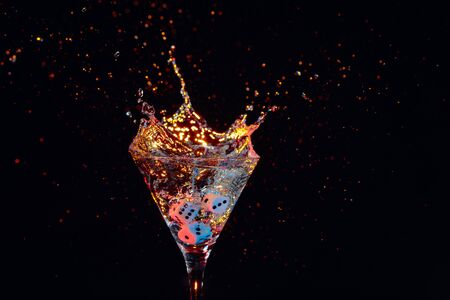 Dice fall in a glass of martini. Colourful cocktail in glass with splash on the dark background. Copy space.の写真素材