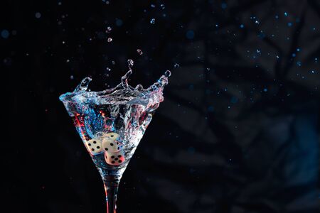 Dice fall in a glass of martini. Colourful cocktail in glass with splash on the dark background. Copy space.の写真素材