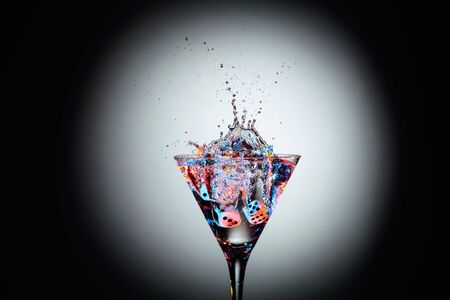 Dice fall in a glass of martini. Colourful cocktail in glass with splash on the dark background. Copy space.の写真素材