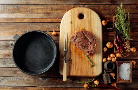 Uncooked steak in sauce with spices an rosemary on a old wooden table. Top view.の写真素材