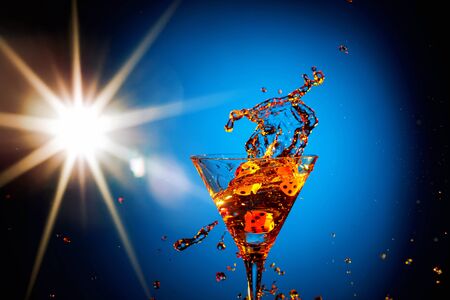 Dice fall in a glass of martini. Colourful cocktail in glass with splash on the blue background. Copy space.の写真素材