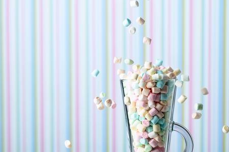 Marshmallows fall in mug. Small colorful marshmallows in glass mug on a striped background. Copy space.の写真素材
