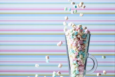 Marshmallows fall in mug. Small colorful marshmallows in glass mug on a striped background. Copy space.の写真素材