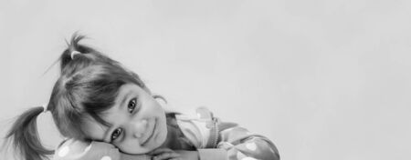 Portrait of a cute little girl with pigtails. The cute little girl has her head in her hands and is...