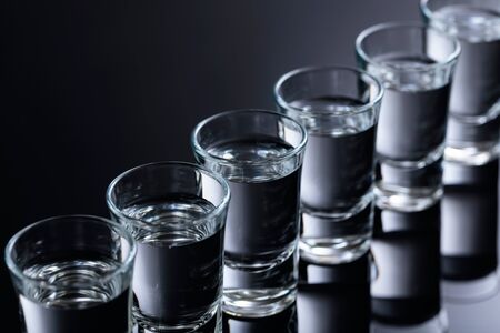 Glasses of vodka on a black reflective background. Selective focus.の写真素材