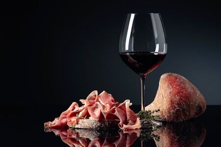 Prosciutto with ciabatta, red wine and thyme on a black reflective background.  Copy space.の写真素材