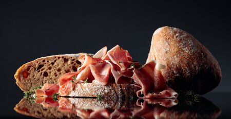Prosciutto with ciabatta and thyme on a black reflective background.の写真素材