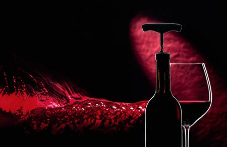Bottle with corkscrew and glass of red wine on a dark background. Free space for your text.の写真素材